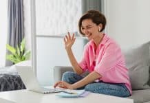 woman in pink shirt sitting relaxed on sofa at home at table working online on laptop
