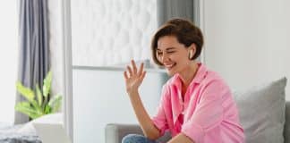 woman in pink shirt sitting relaxed on sofa at home at table working online on laptop