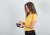 Young woman taking money out of wallet in yellow t shirt, black pants .