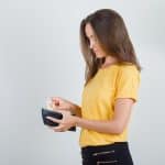 Young woman taking money out of wallet in yellow t shirt, black pants .