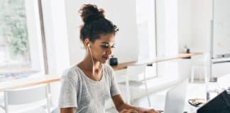 Romantic african girl with trendy hairstyle sitting at her workplace and analysing data. Indoor portrait of black female student working with laptop before exam..