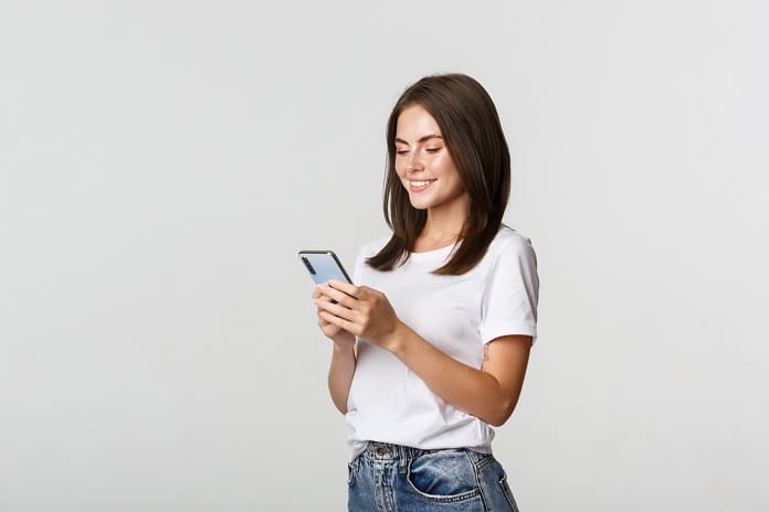 Beautiful smiling girl using mobile phone, looking at smartphone pleased